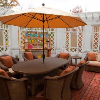 A cozy outdoor patio with a large table, cushioned seating, and an umbrella.
