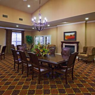 A well-furnished dining or conference room featuring a large table with chairs, a chandelier, a fireplace, and decorative elements such as a painting and flowers.