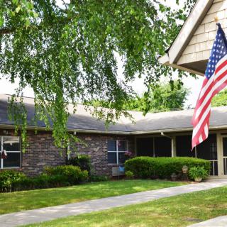 A suburban brick house with an American flag on display and a well-kept lawn.