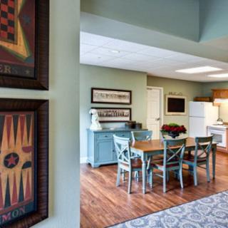 A cozy dining area with a wooden table and chairs, adjacent to a kitchen, featuring framed artwork on the wall.