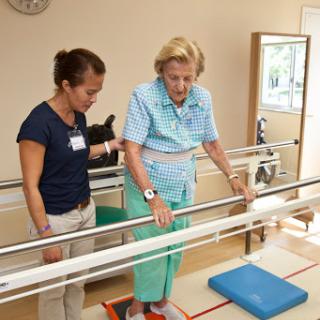 An elderly woman receiving assistance from a therapist during a physical therapy session focused on improving balance and mobility.
