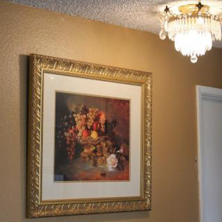 A still life painting in a gold frame adorns a wall beneath an elegant light fixture.