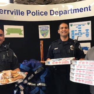 Police officers holding pizza boxes and sandwiches at an event.