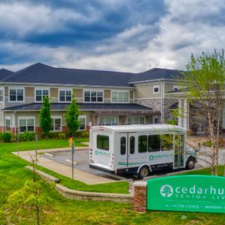 A modern building with a bus parked outside, surrounded by green landscaping and a cloudy sky.