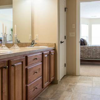 A bathroom featuring a wooden vanity with a mirror and decorative candles, leading into a bedroom.