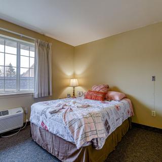 A cozy bedroom with a neatly made bed, soft lighting, and a large window.