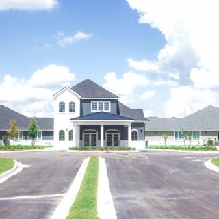 A large residential building with a spacious driveway under a partly cloudy sky.