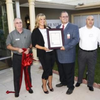 A group of people participating in a ribbon-cutting ceremony, with one person holding a certificate.