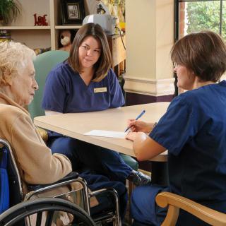 Healthcare professionals engage in a conversation with an elderly person in a wheelchair at a nursing home.
