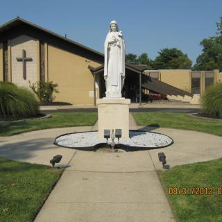 A religious statue in front of a church building on a sunny day.