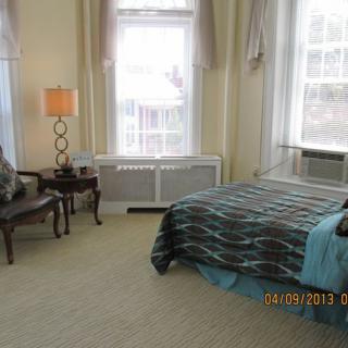 A traditional bedroom with a bed, chair, and lamp by the window.