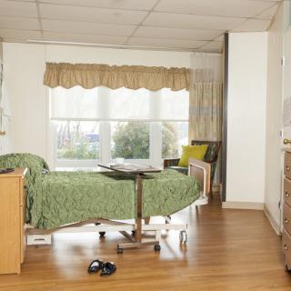 A well-lit hospital room with a single bed, window, and wooden flooring.
