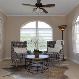 A cozy living room setup with two patterned chairs and a round coffee table, adorned with an orchid centerpiece, under large arched windows and a ceiling fan.