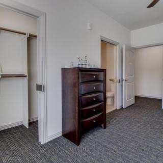 An empty bedroom with a dresser and open closets.