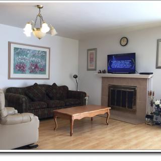 A cozy living room featuring a sofa, armchair, and coffee table, with a fireplace and television mounted above it.
