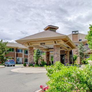 A welcoming building entrance surrounded by lush greenery under a cloudy sky.