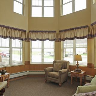 A cozy living room with large windows, armchairs, and a lamp.