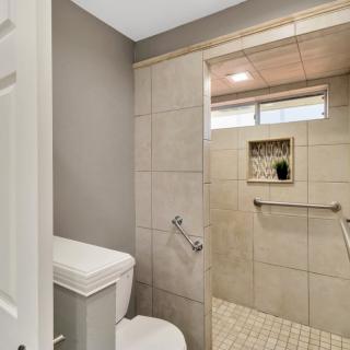 A modern bathroom featuring a walk-in shower with grab bars and neutral-toned tiles.