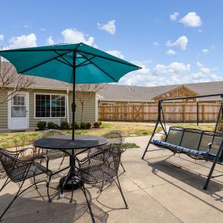A cozy backyard patio featuring a table with chairs and an umbrella, alongside a comfortable swing.
