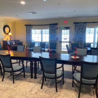 A spacious dining area with a large table and multiple chairs, featuring natural light from the windows and elegant decor.