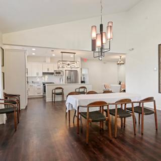 A modern open-concept dining and kitchen area featuring wood flooring, a contemporary chandelier, and stylish furniture.