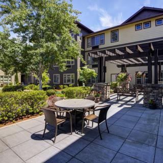 A cozy outdoor patio with tables and chairs surrounded by lush greenery and adjacent to a building.
