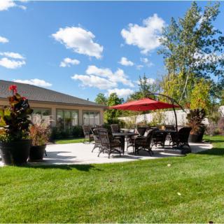 A sunny outdoor patio with seating and a red umbrella overlooking a well-maintained lawn.