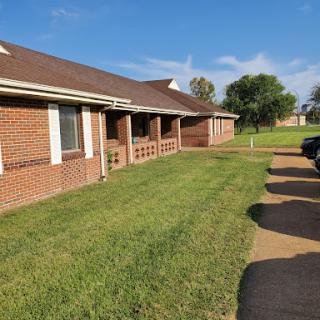 A sunny view of a brick residential building with well-maintained grass and a clear blue sky.