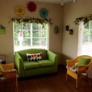 A cozy living room with a green couch and yellow chairs, featuring colorful decorations and ample natural light from the windows.