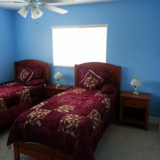 A cozy bedroom with two twin beds and blue walls, featuring nightstands and table lamps under a ceiling fan.