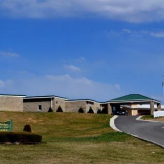 A scenic view of a modern building complex with a winding driveway under a blue sky with clouds.