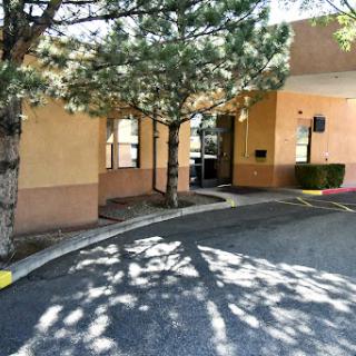 A view of a business entrance surrounded by trees and casting shadows on the pavement.