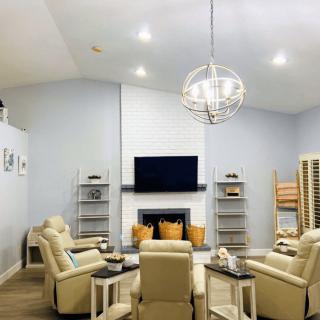 A modern living room with cream chairs, a central fireplace, and a large television.