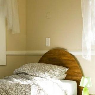 A cozy bedroom corner with a bed, a small lamp, and sheer curtains letting in natural light.