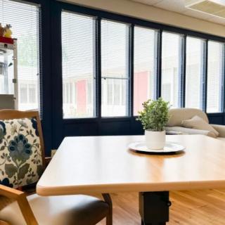 A cozy living room with a wooden table, a potted plant, and comfortable seating near large windows.