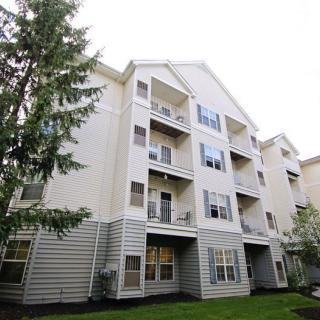 A multi-story apartment building with balconies, surrounded by trees and grass.