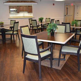 A well-arranged dining room with multiple tables and chairs, featuring decorative plants on polished hardwood flooring.