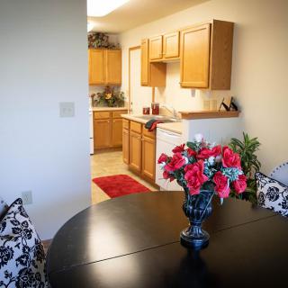 A cozy dining area with a black table and floral centerpiece, leading into a warm kitchen space.