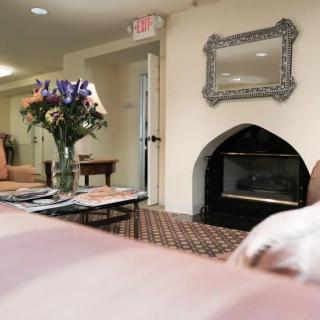 A cozy living room featuring a fireplace, elegant mirror, and a coffee table with a vase of flowers.