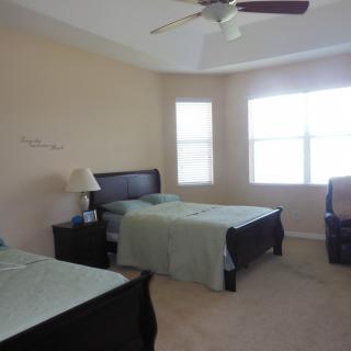 A spacious bedroom with two twin beds, a nightstand with a lamp, and large windows that let in natural light.