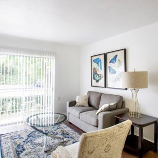 A bright and modern living room with a sofa, glass coffee table, and decorative artwork on the wall.