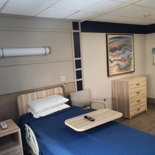 A neatly arranged hospital room featuring a bed, a side table, and a painting on the wall.