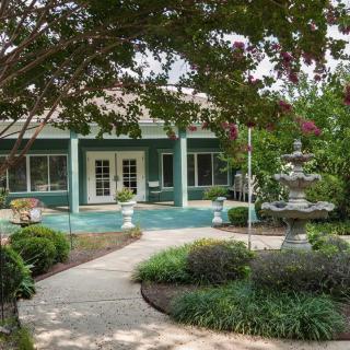 A scenic garden path leads to a charming building, surrounded by lush greenery and featuring a decorative fountain.