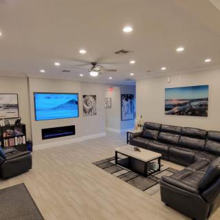 A modern living room featuring a large sectional sofa, a flat-screen TV, wall art, and recessed lighting.