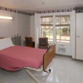 A hospital room with a single bed, chairs, and large windows.