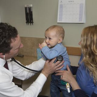 A doctor examines a baby with a stethoscope while the mother holds the child during a medical appointment.