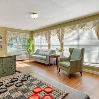 A cozy living room with large windows, comfortable seating, and a checkers game set up on the table.
