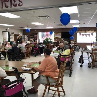 A group of people gathered in a community center decorated with blue balloons.