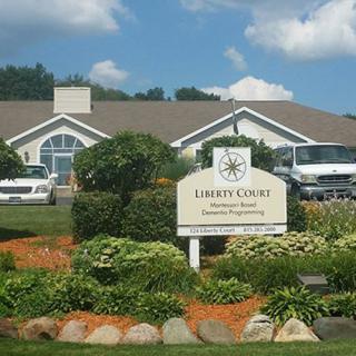 A commercial building with a landscaped garden and a sign for Liberty Group, featuring parked vehicles in the background.