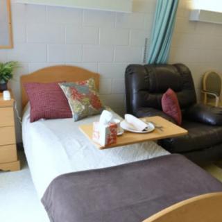 A cozy hospital room with a bed, side chair, and tray table.